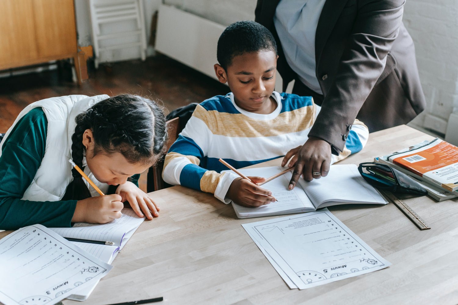 A teacher helps two young students with school work